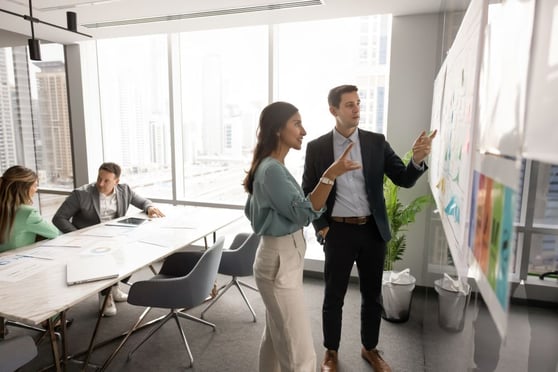 Business colleagues speaking at Kanban board with sticky notes.