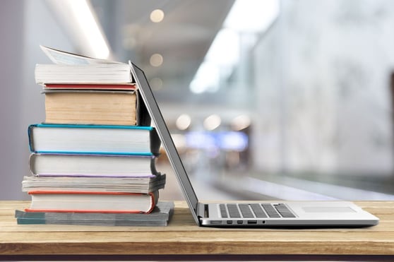 Stack of books with laptop on wooden table.