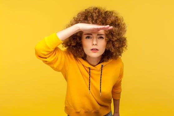Woman in a yellow sweater with her hand to her forehead, peering into the future.