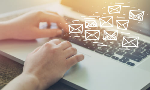 Hands typing on a laptop with flying email icons, representing targeted email marketing for your business.